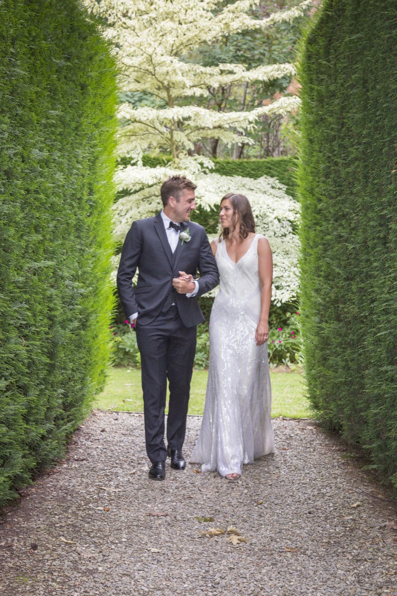 Bride and groom walking hand in hand between tall hedges