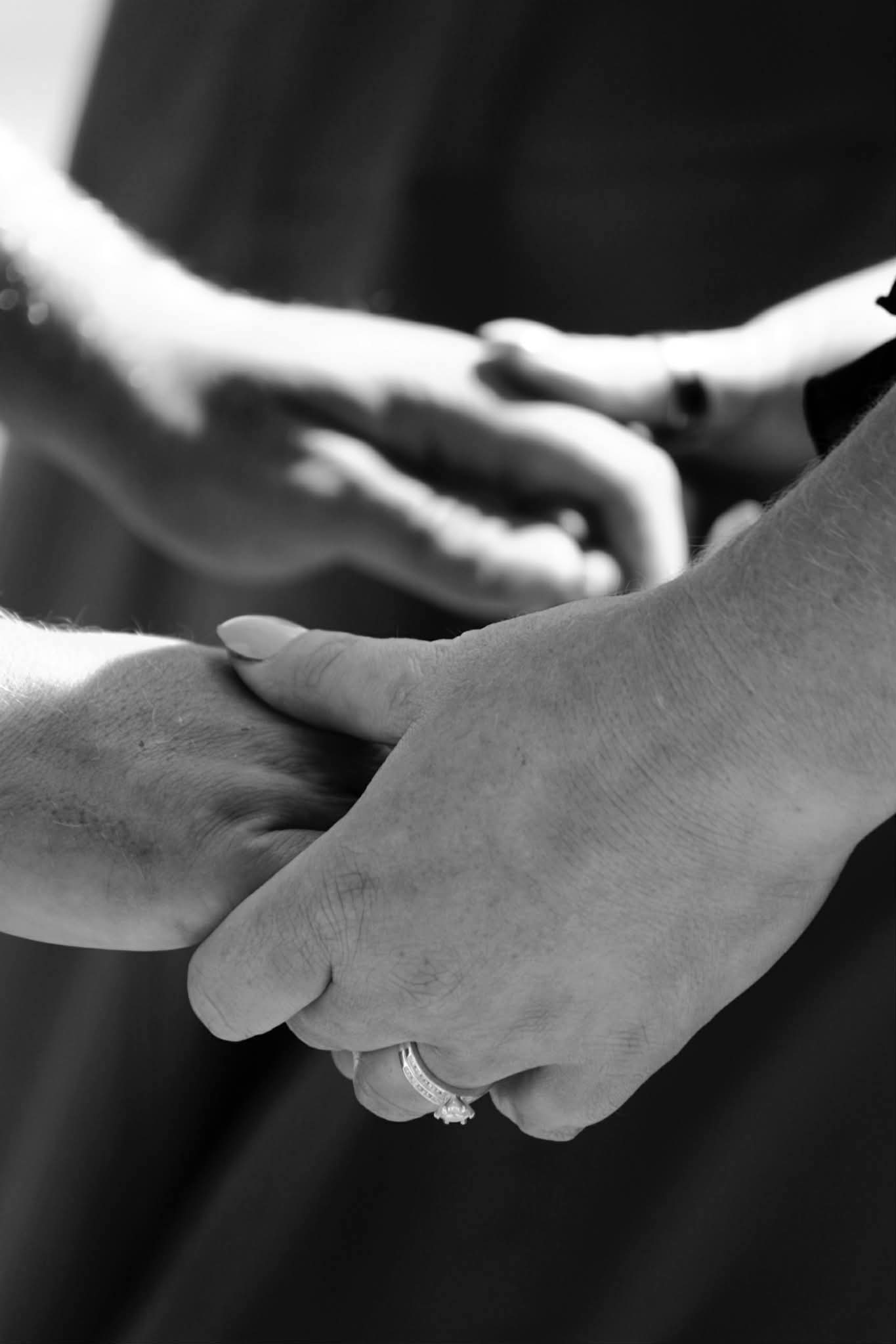 Black and white close-up of a couple holding hands showing a wedding ring